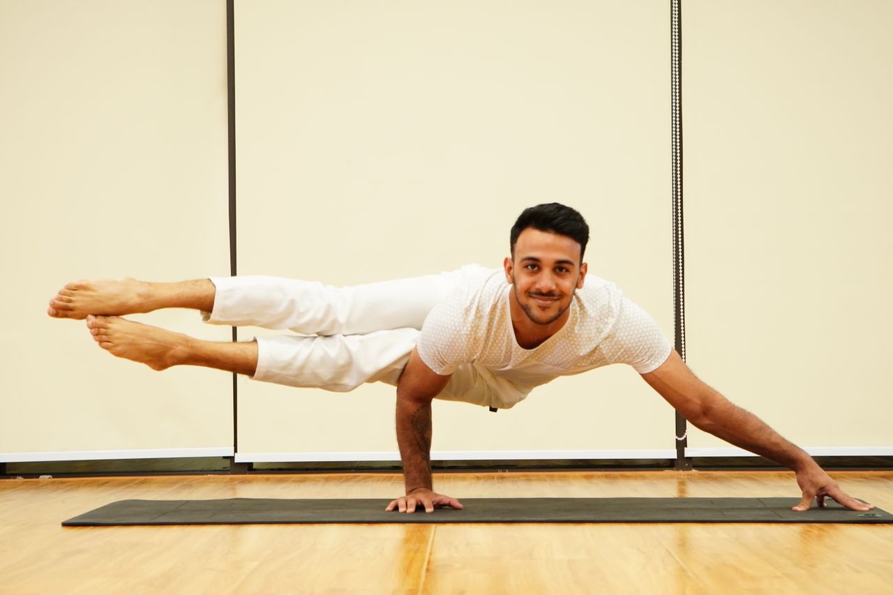 A man balances in an advanced yoga pose on a mat indoors, showcasing strength and focus.